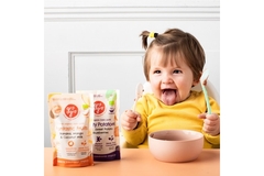 Image Happy toddler eating organic baby food with spoon, sitting at table with GroGro fruit and sweet potato baby food pouches